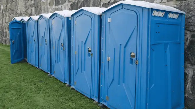 Row of blue portable toilets lined up on grass against a stone wall for event sanitation in Fresno, CA
