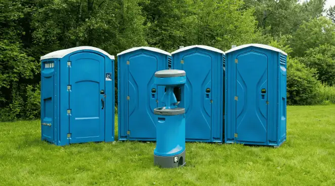 Four blue portable toilets and a matching hand washing station on grass near trees, a common sight at local outdoor events in Fresno, CA