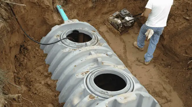 Septic tank installation showing a technician compacting soil around a new poly septic tank in an excavation pit in Fresno, CA